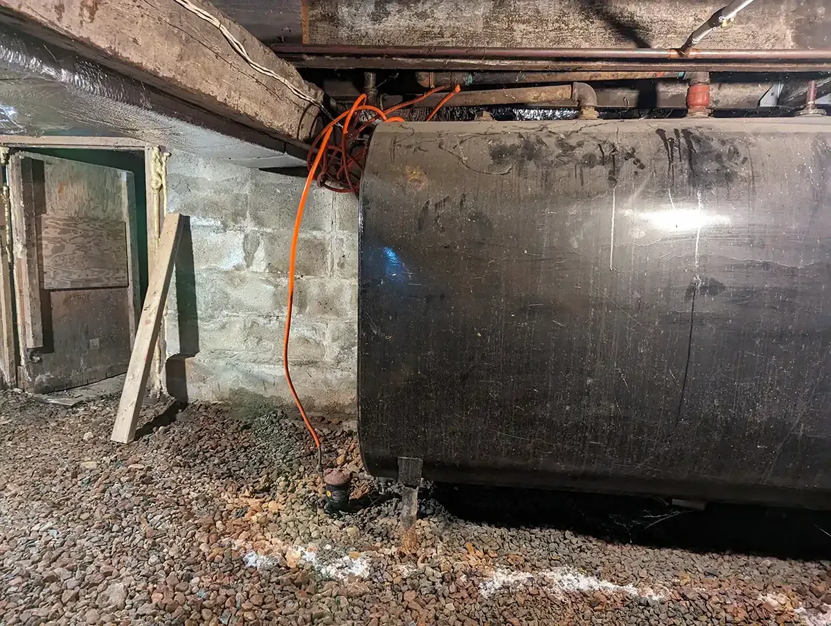 Dim basement with a large black cylindrical tank, red cables, and debris on the floor.