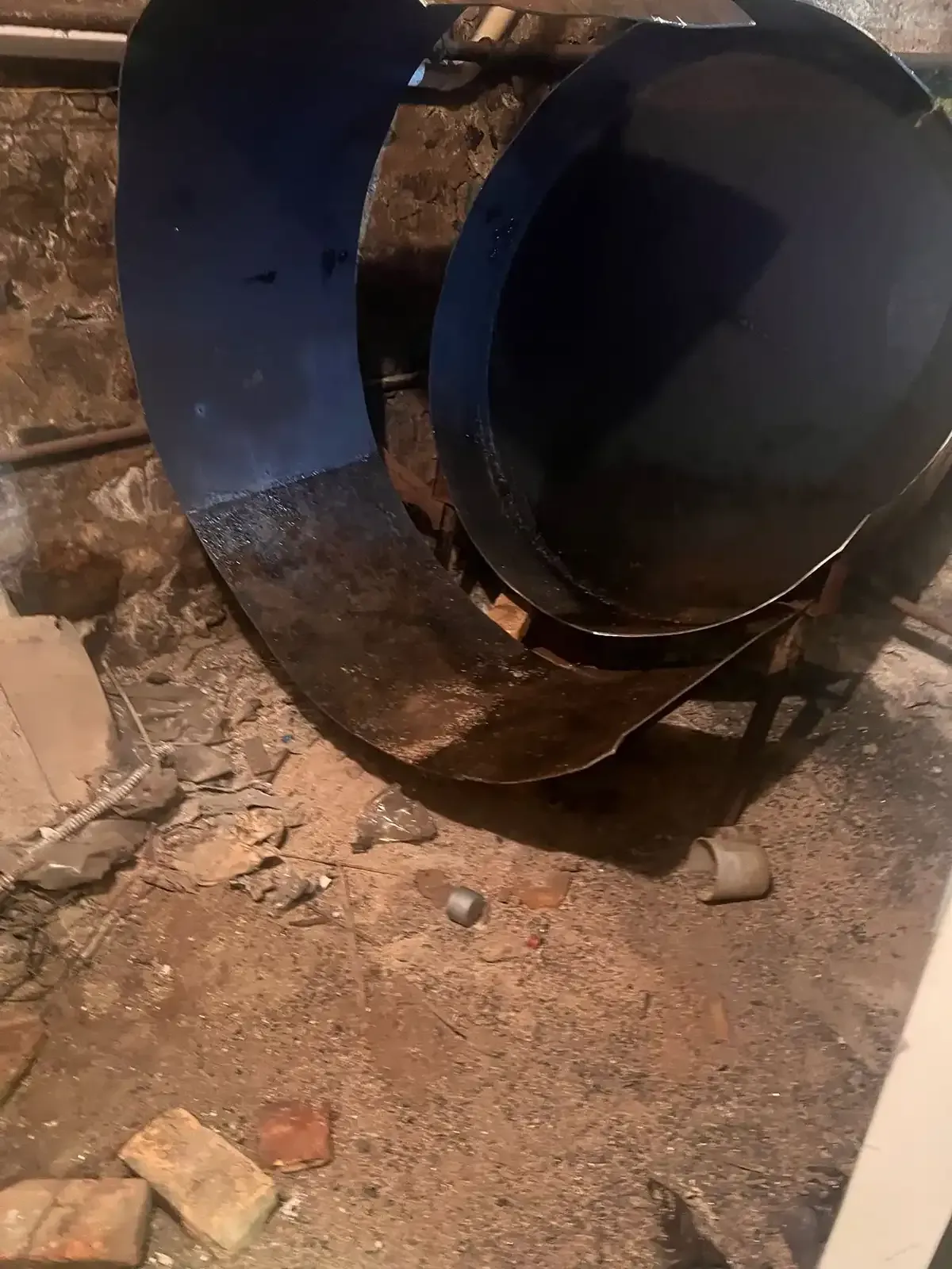 Large blue metal pipe section lying on dirt and debris outdoors.