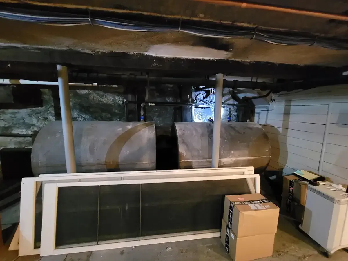 Basement storage area with pipes, furnace, stacked doors, and boxes in a dimly lit room.