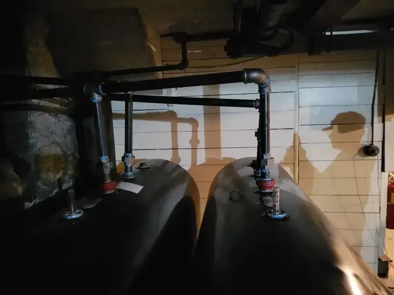 Two black industrial tanks connected by black metal piping in a dimly lit basement.