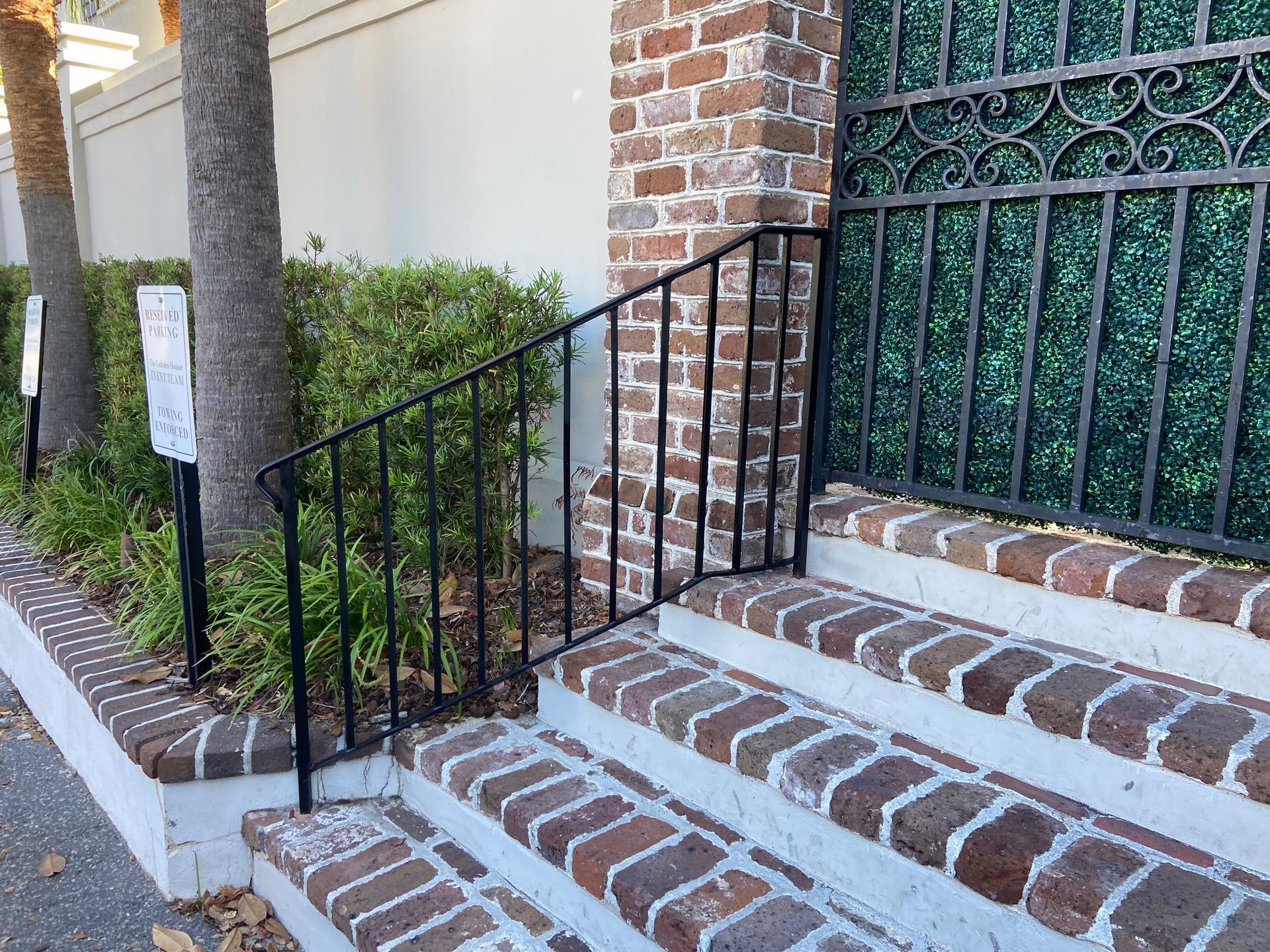 Brick steps with black railing leading to a brick and iron gate entrance.