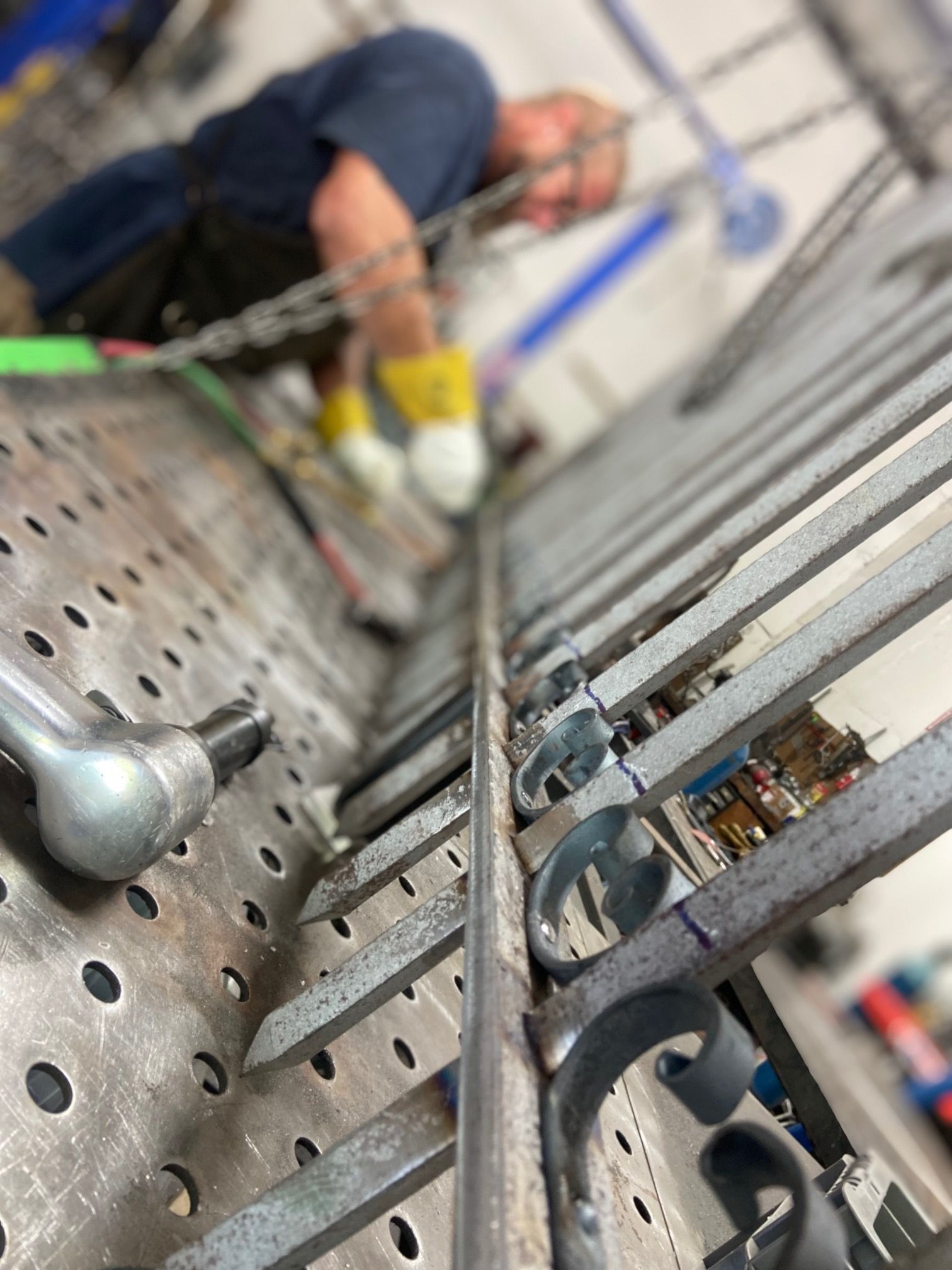 A person welding metal railing on a perforated workbench. The person wears gloves and safety glasses.