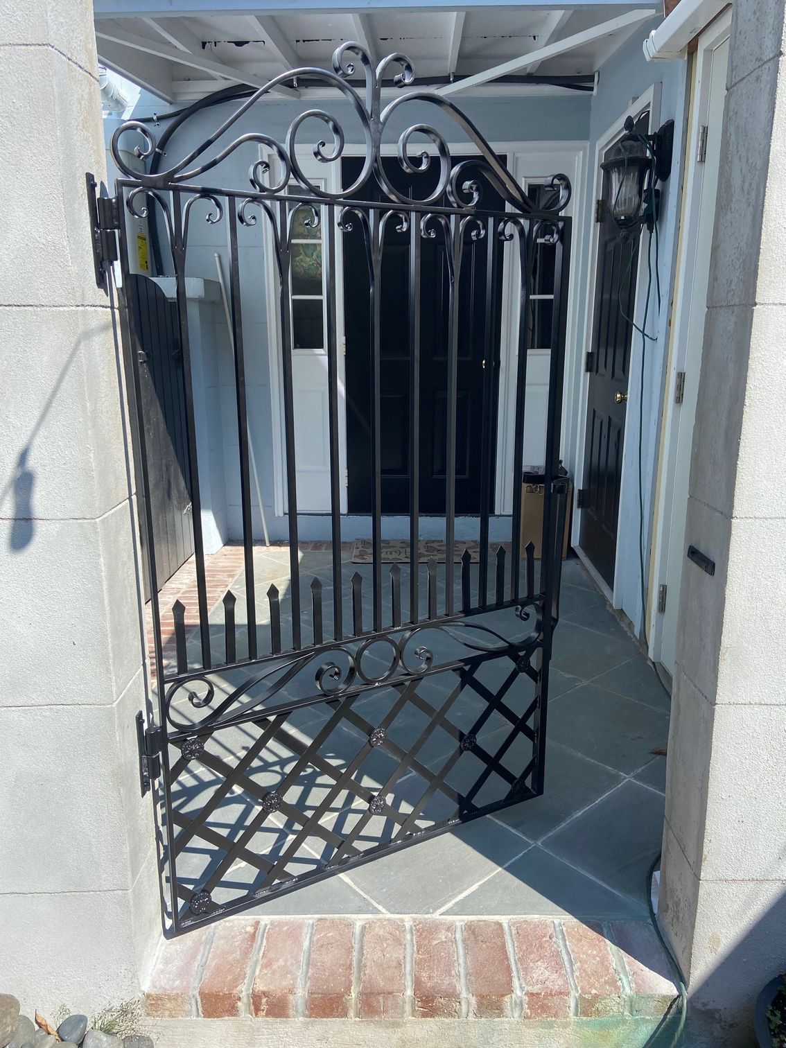 Black wrought-iron gate ajar, leading to a light-filled doorway. Brick and stone path.