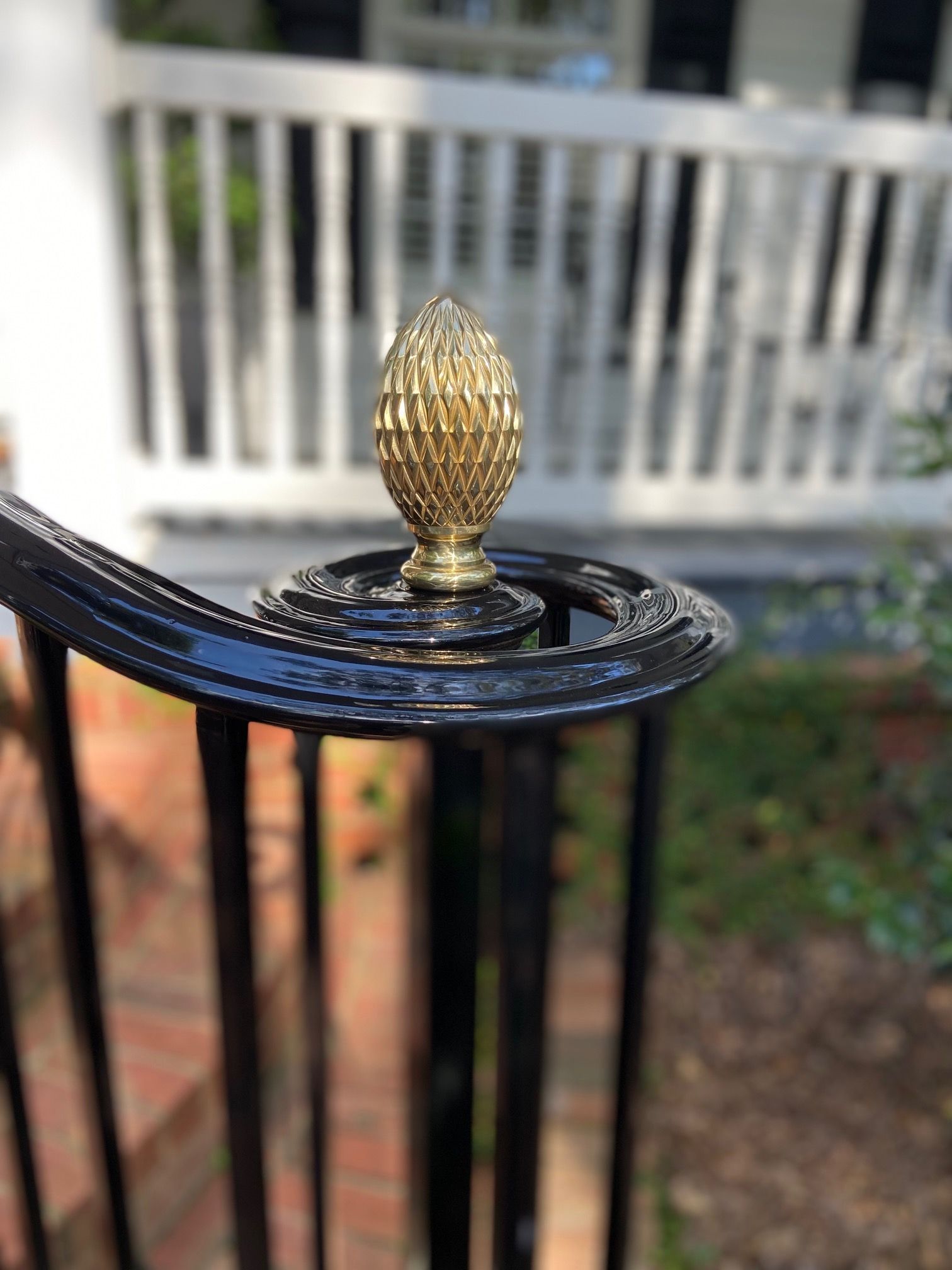 Close-up of a black wrought iron railing with a decorative gold finial in front of a house with a white porch.