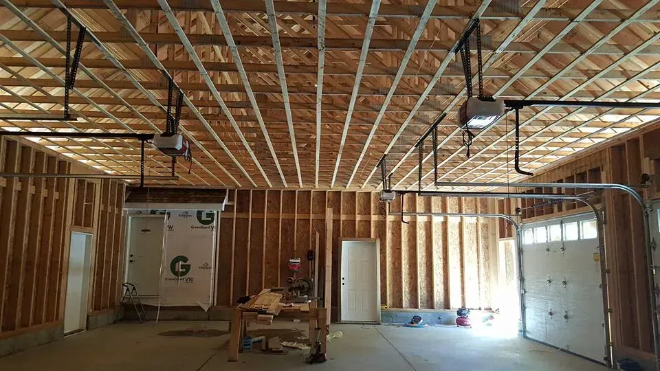 Interior view of a wood-framed garage under construction with exposed ceiling beams and garage door openers.