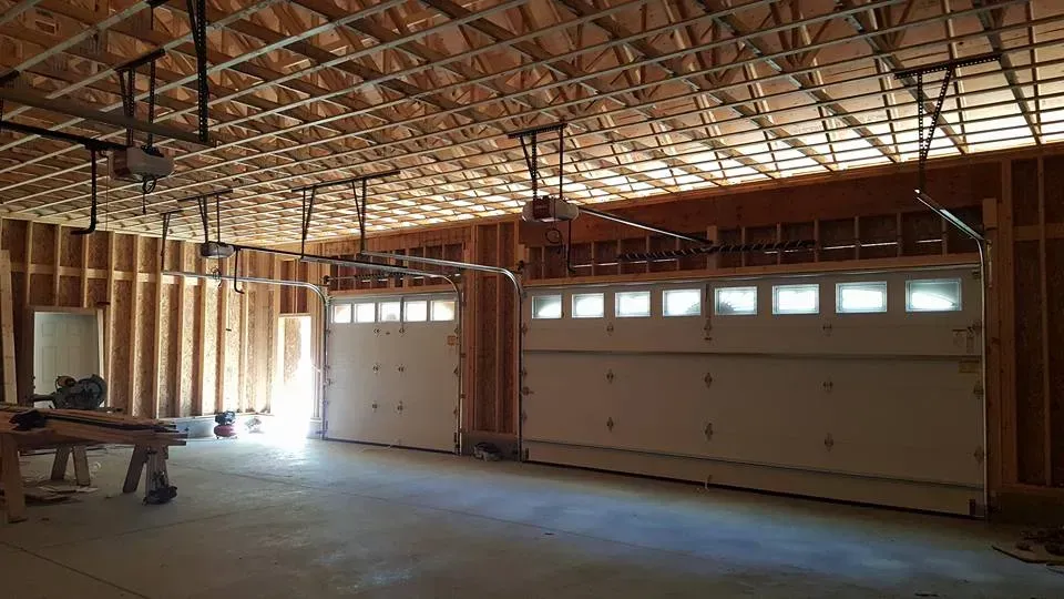 Unfinished garage interior with two white garage doors and exposed wooden beams.