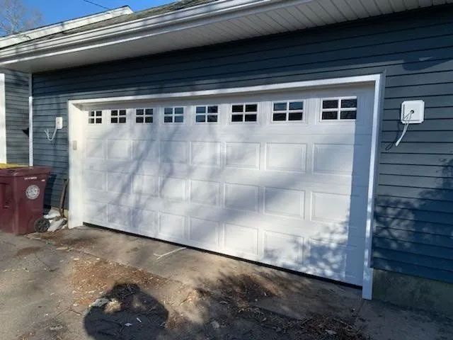 White garage door with small window panes above, on a blue house.