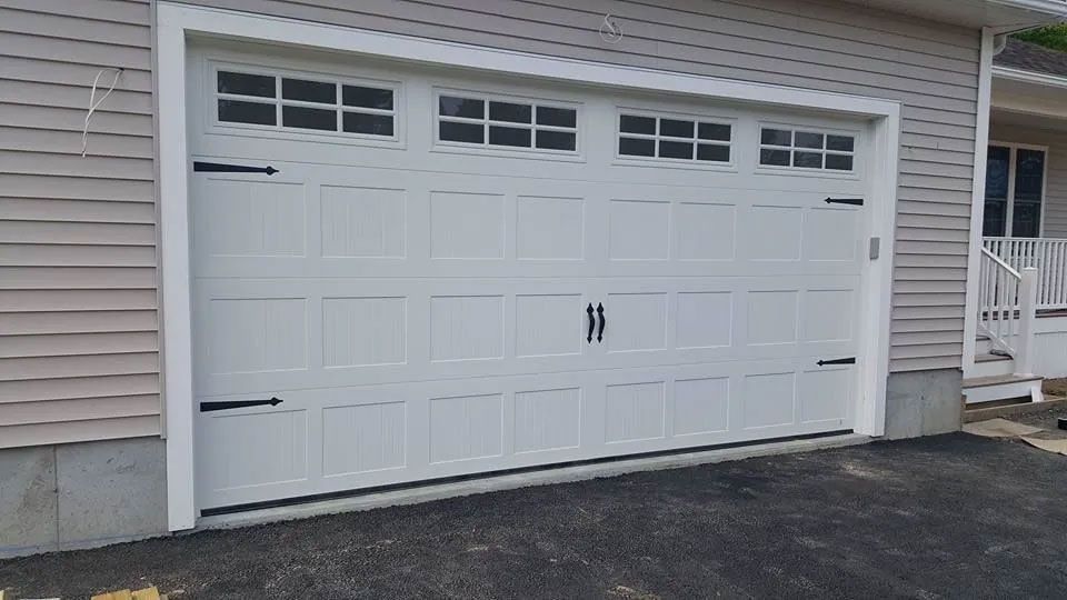 White garage door with decorative black hardware, with windows above. Building exterior.