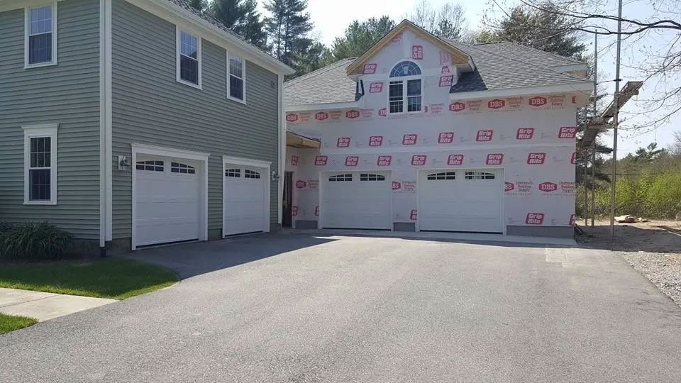 Two-story house with attached garage under construction, asphalt driveway, and grass lawn.