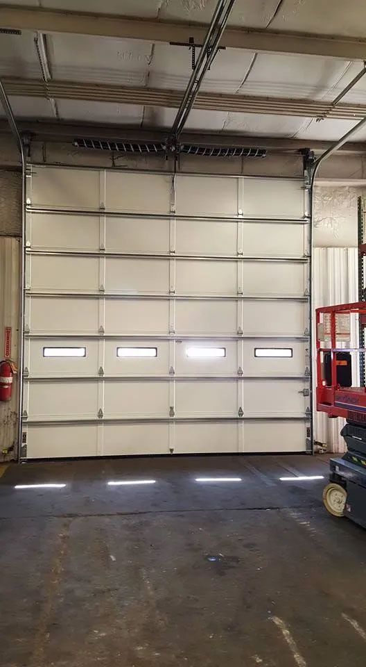 White industrial garage door with three rectangular windows, inside a warehouse.
