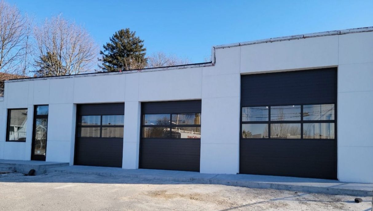 White commercial building with three dark gray garage doors and a small glass entrance.