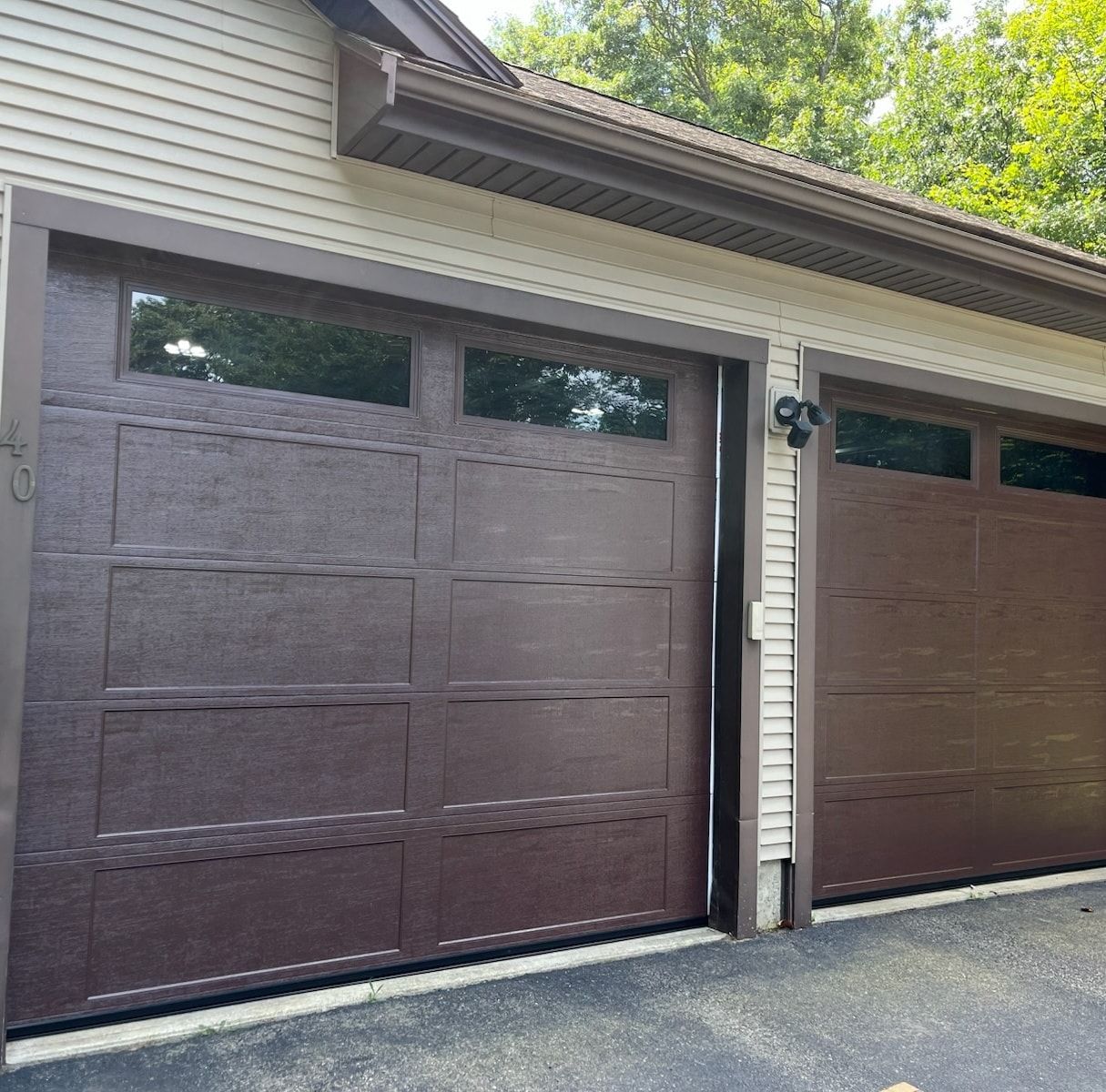 Brown garage doors with windows, set in a brown frame, against beige siding.