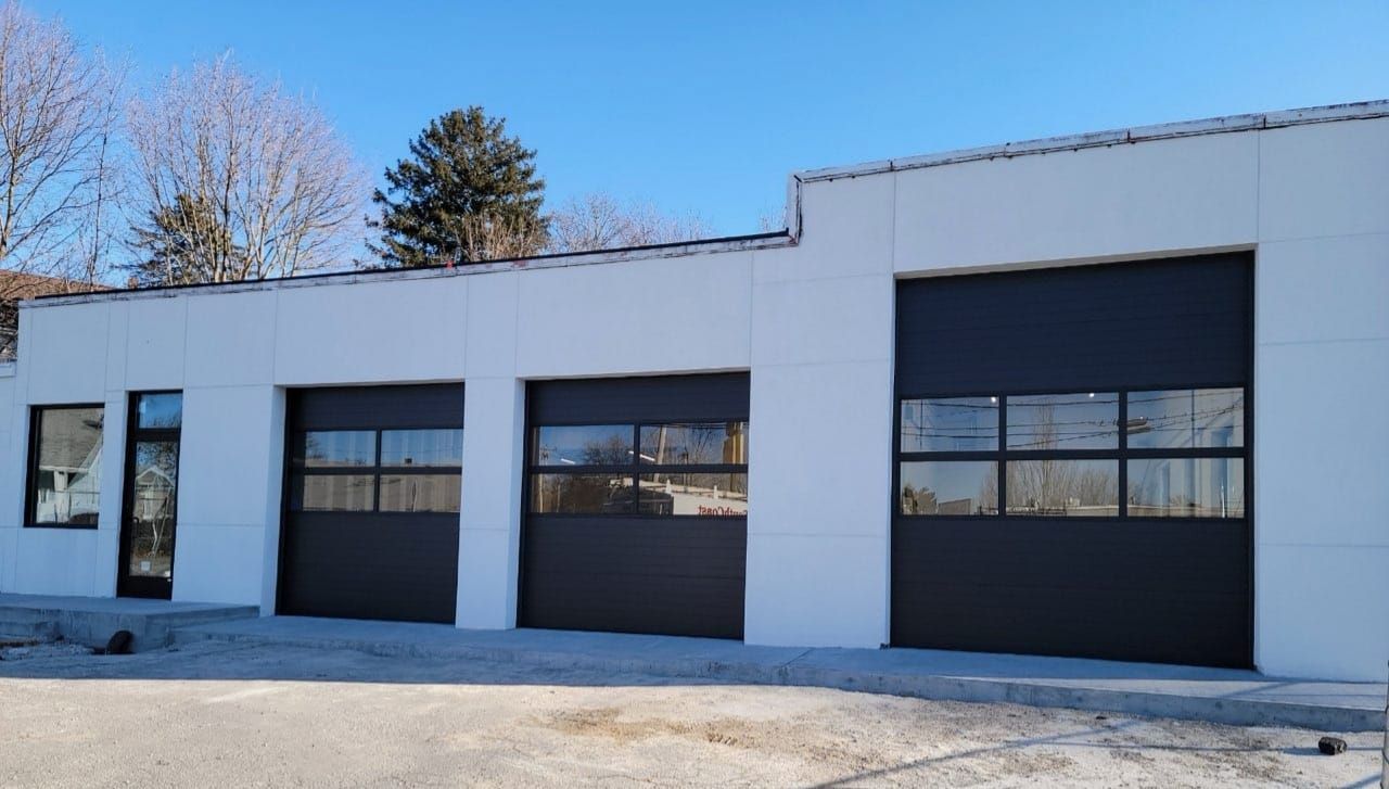 White building with three dark garage doors, under a clear blue sky.