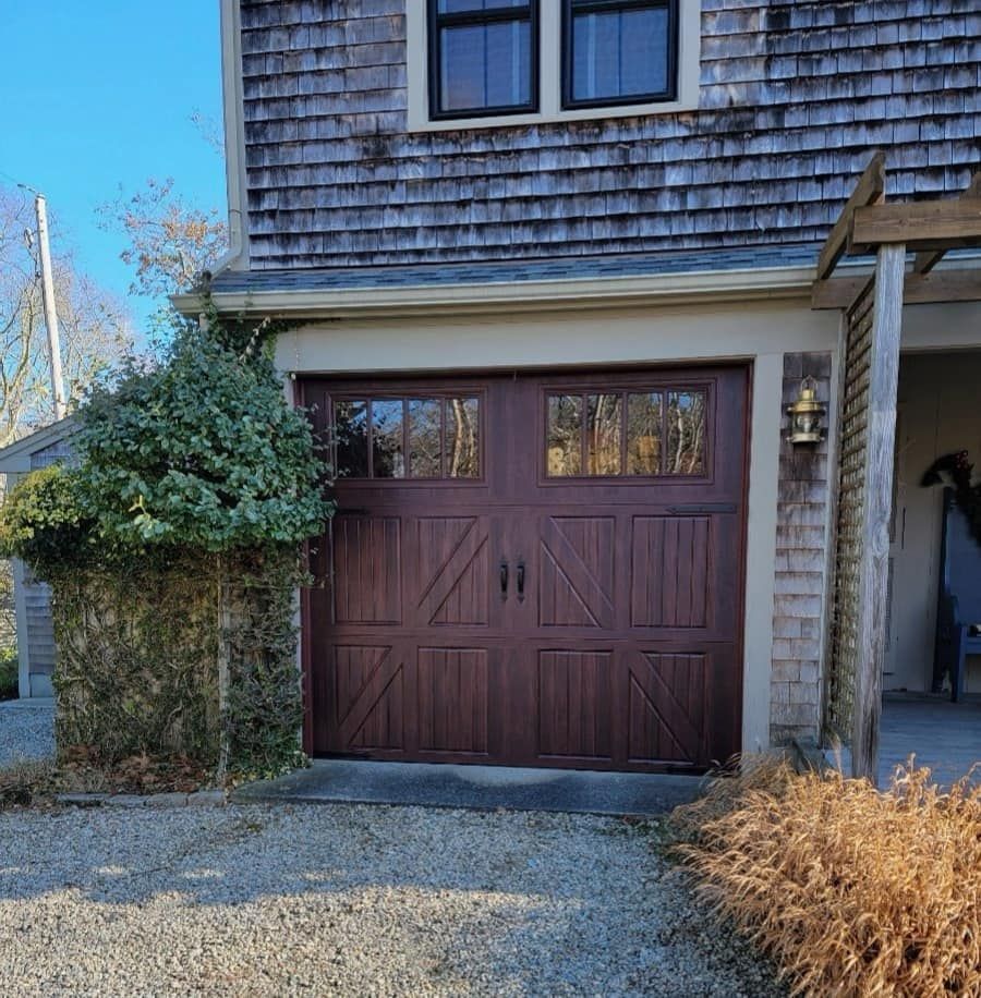 Brown garage door with windows, next to a house with weathered shingles.