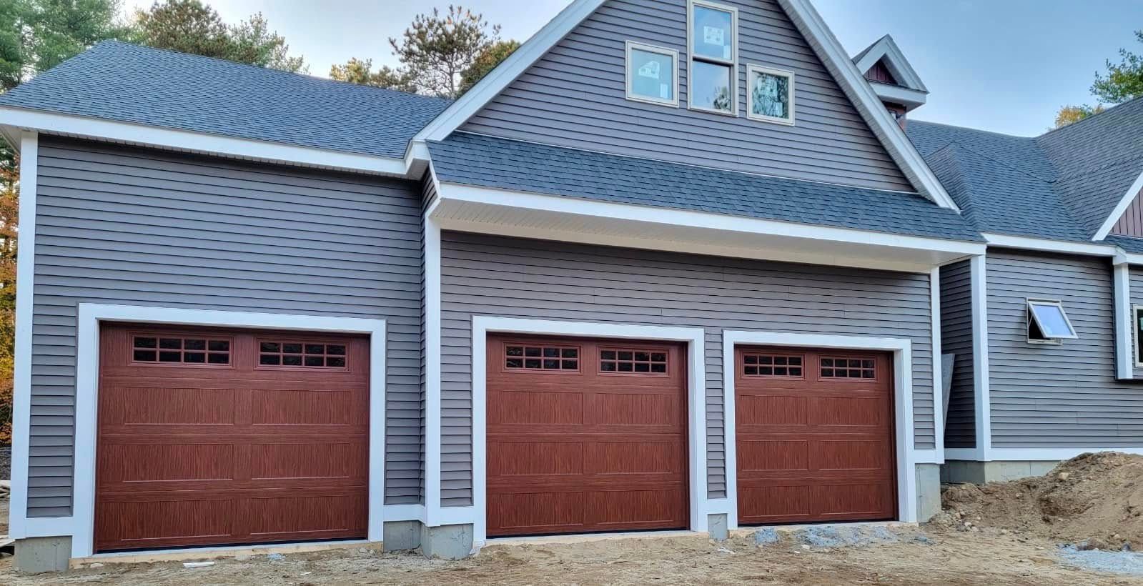 Three-car garage with brown doors, grey siding, and white trim; newly built home.