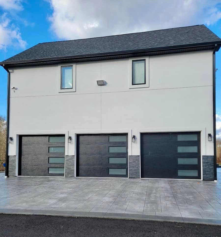Three-bay garage with dark gray doors and light gray exterior, blue sky overhead.