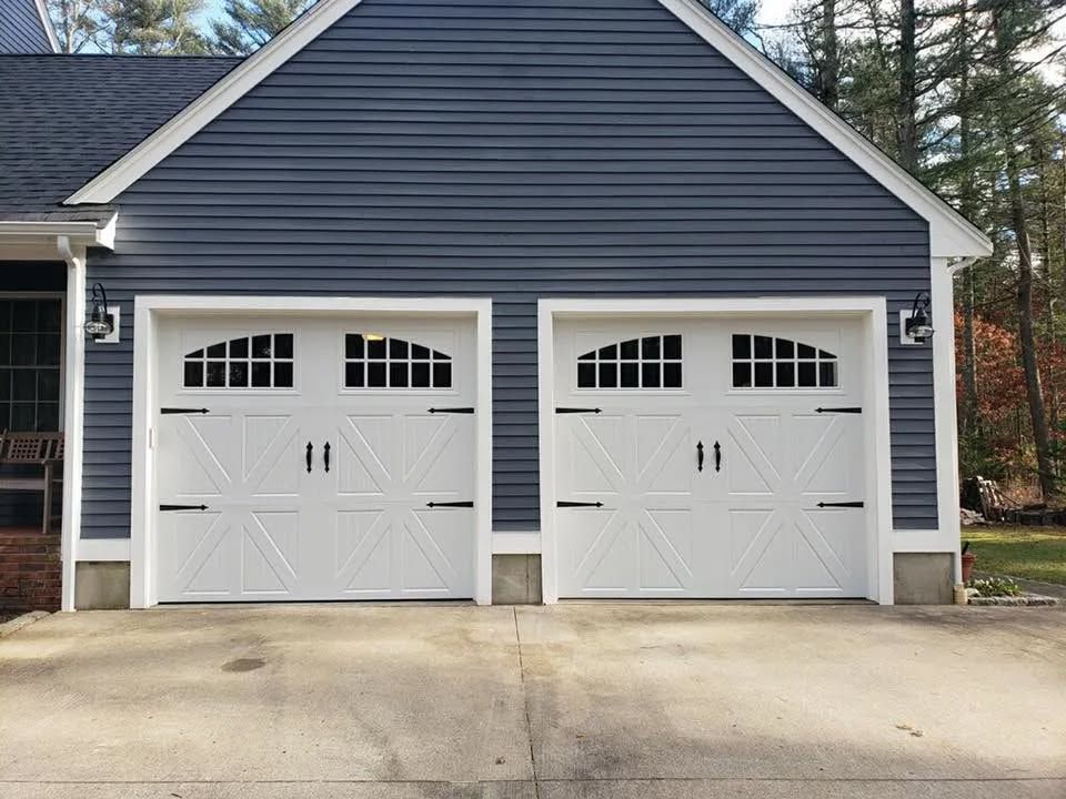 Two white garage doors with arched windows, black hardware, and blue siding.