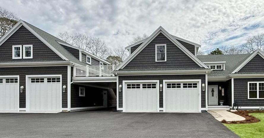 Dark gray house with white garage doors and trim, driveway. Overcast sky.