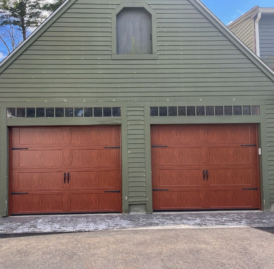 Two-car garage with brown doors and green siding. A small arched window sits at the top of the structure.