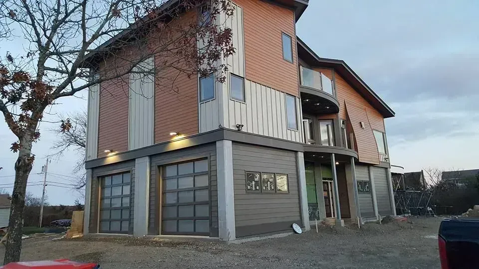 Modern house with glass garage doors, brown and grey siding, and a balcony.