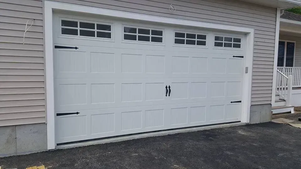 White garage door with black hinges and windows, set in a light grey building.