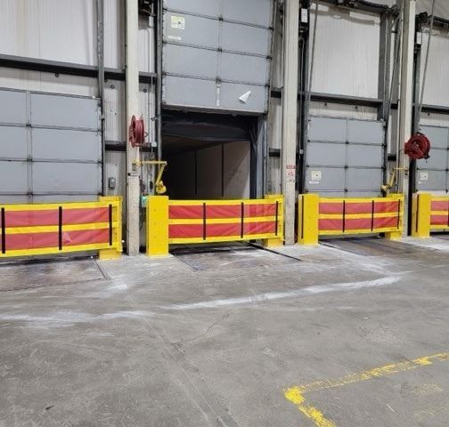 Loading dock with yellow and red safety barriers; closed gray overhead doors.