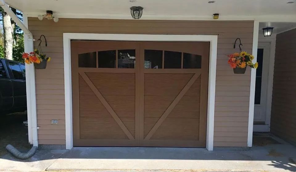 Brown garage door with white trim, hanging flowers, and tan siding.