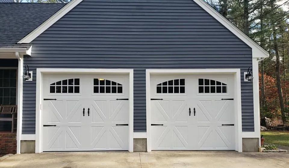 Two white garage doors with black accents, on a blue-sided building.