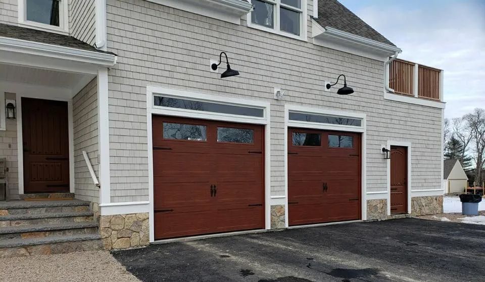 Two-car garage with brown doors, light gray siding, and stone accents. Asphalt driveway with snow.