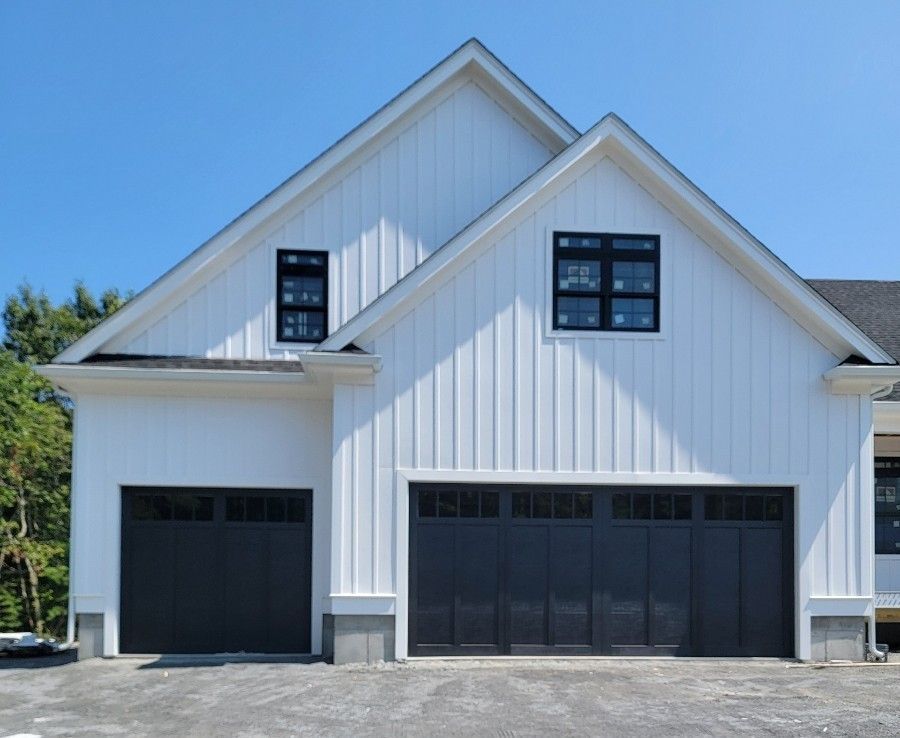 White house with black garage doors, windows, and trim against a blue sky.