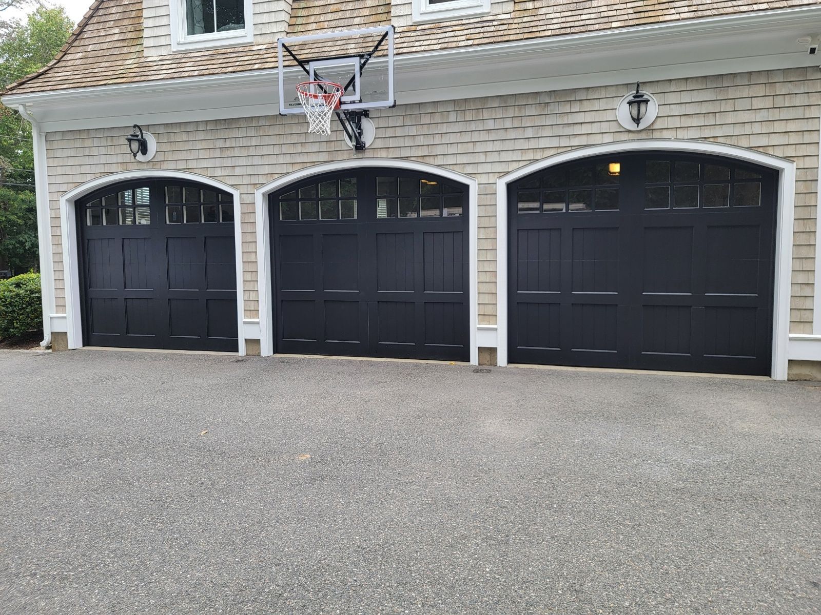 Three black garage doors with arched tops on a light stone facade; basketball hoop above the middle door.