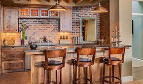 A kitchen with a large island and stools and a brick wall.