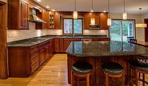 A kitchen with wooden cabinets , granite counter tops , and stools.