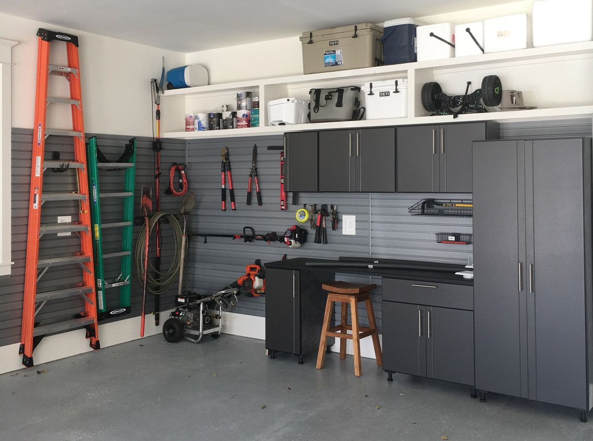 Organized garage storage: Gray cabinets, wall-mounted tools, ladders, and shelves with bins and coolers.