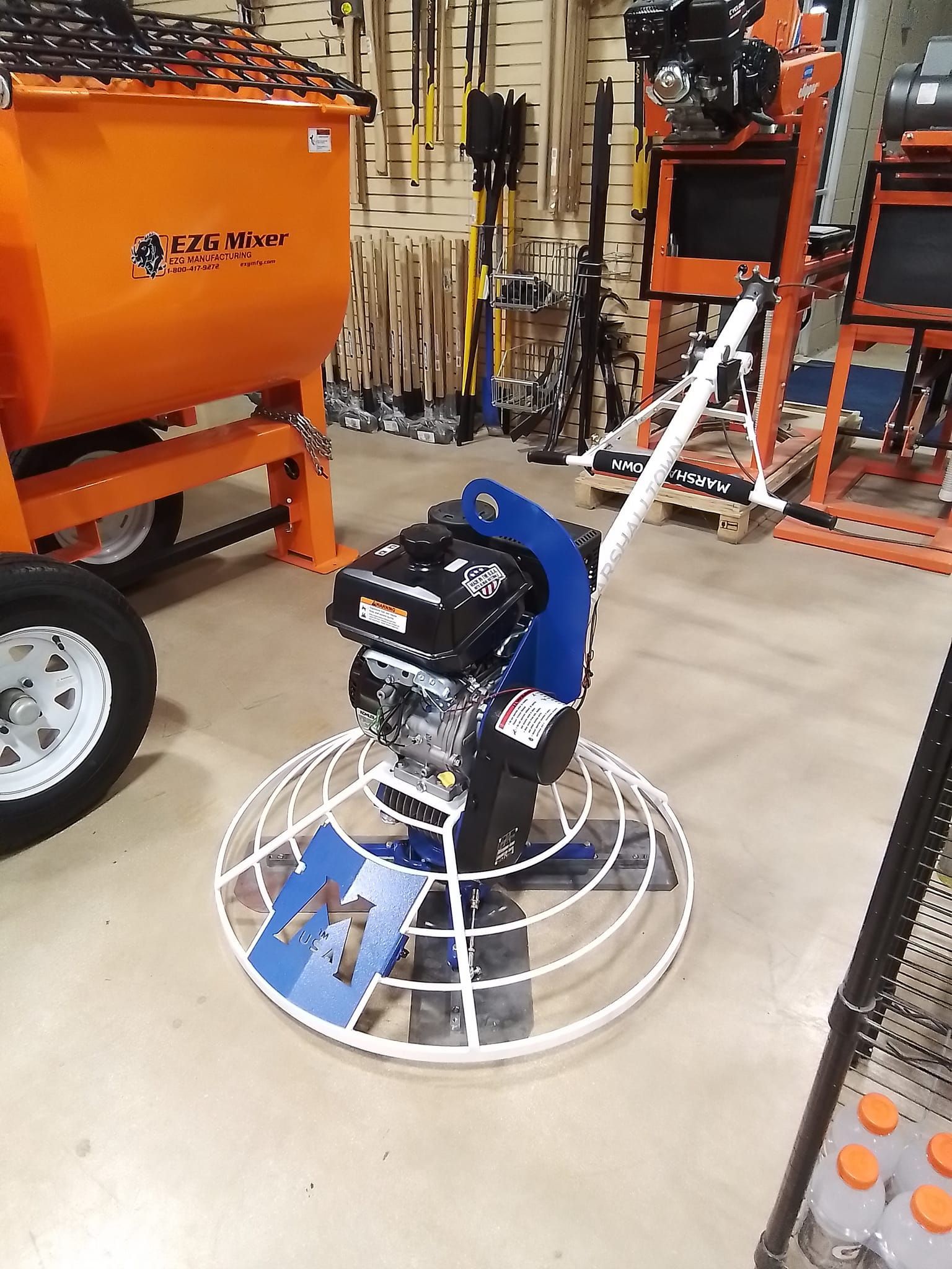 A concrete trowel is sitting in a warehouse next to a mixer.