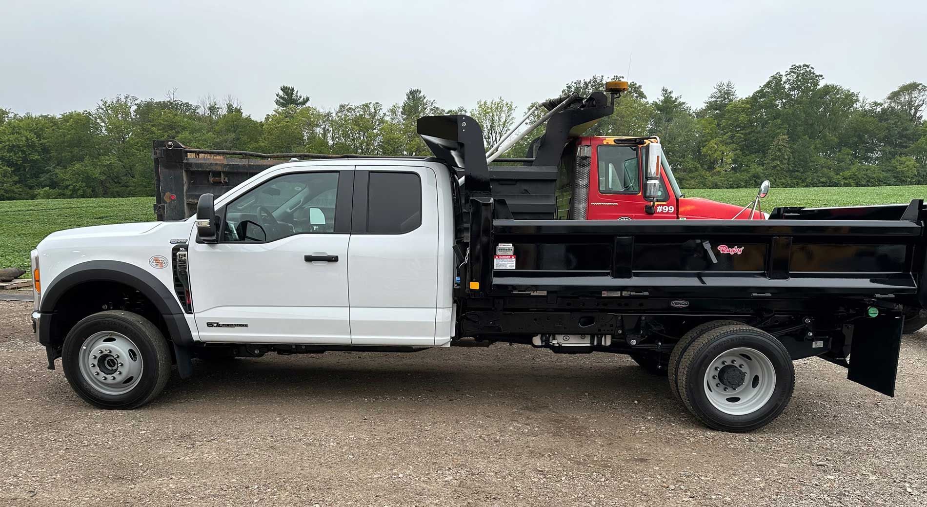White dump truck with black bed, parked outdoors. Red snow blower in the bed.