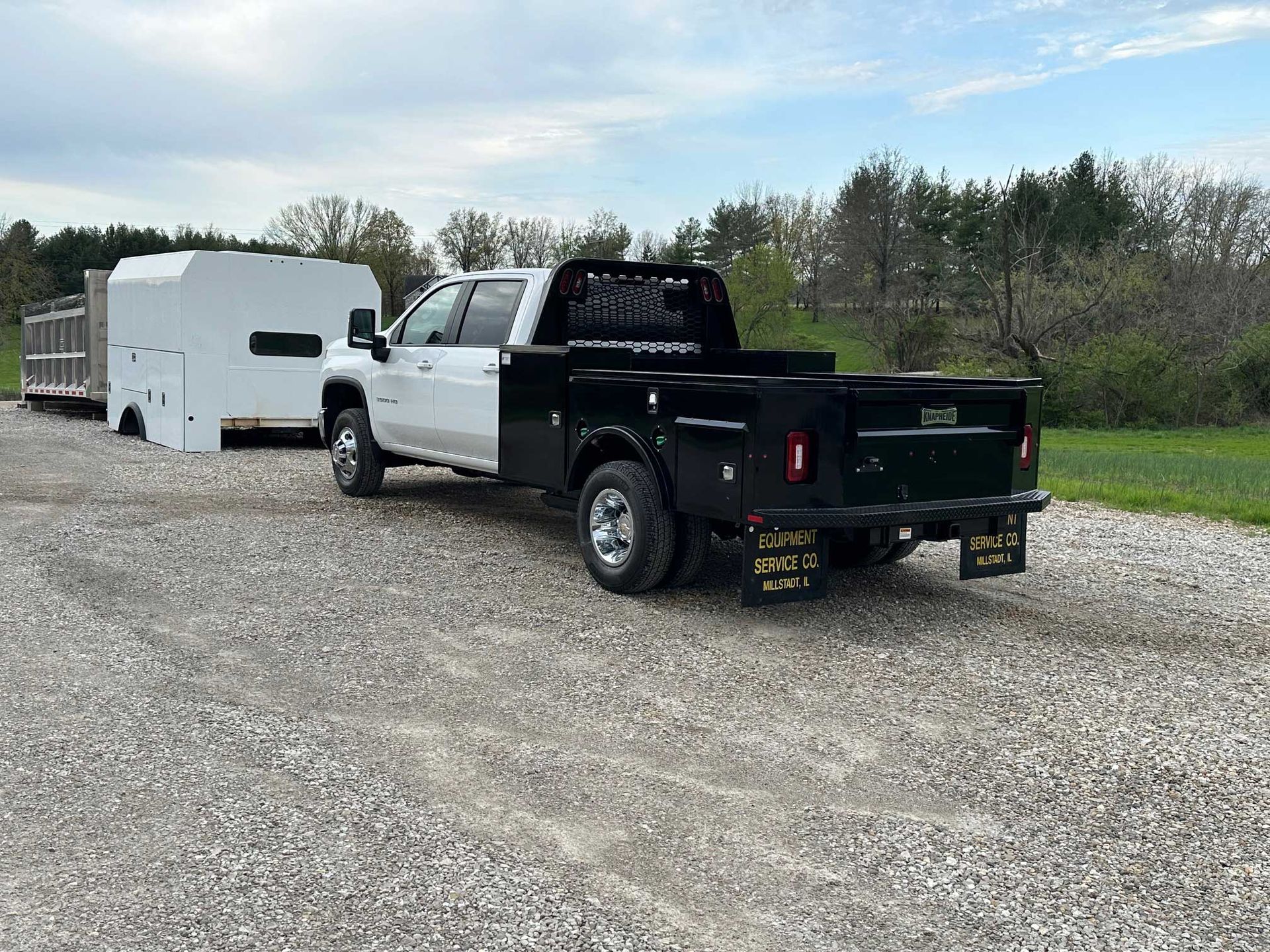 White and black pickup truck with a trailer on a gravel driveway.