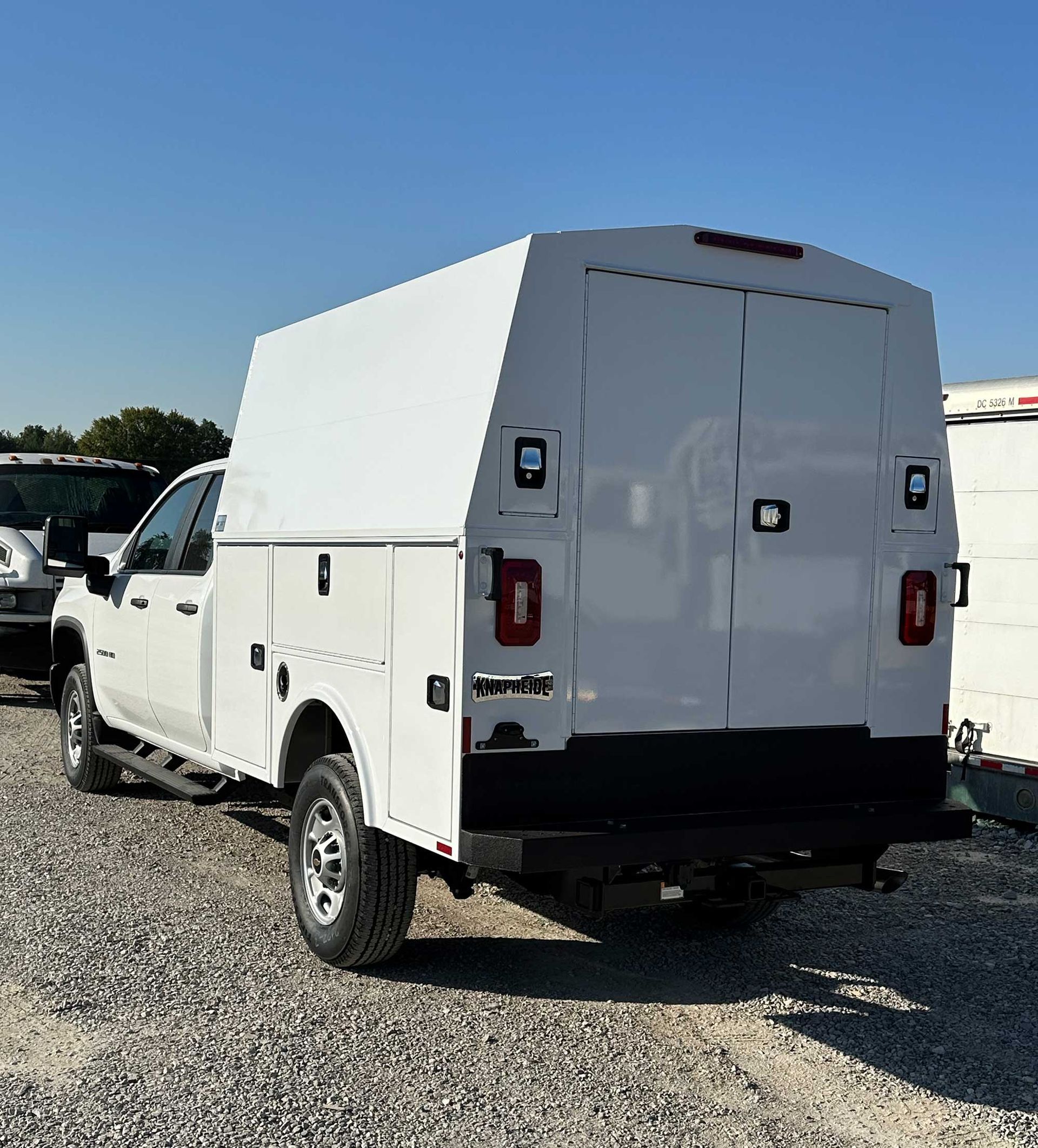 White work truck with utility bed, parked outside on a sunny day.