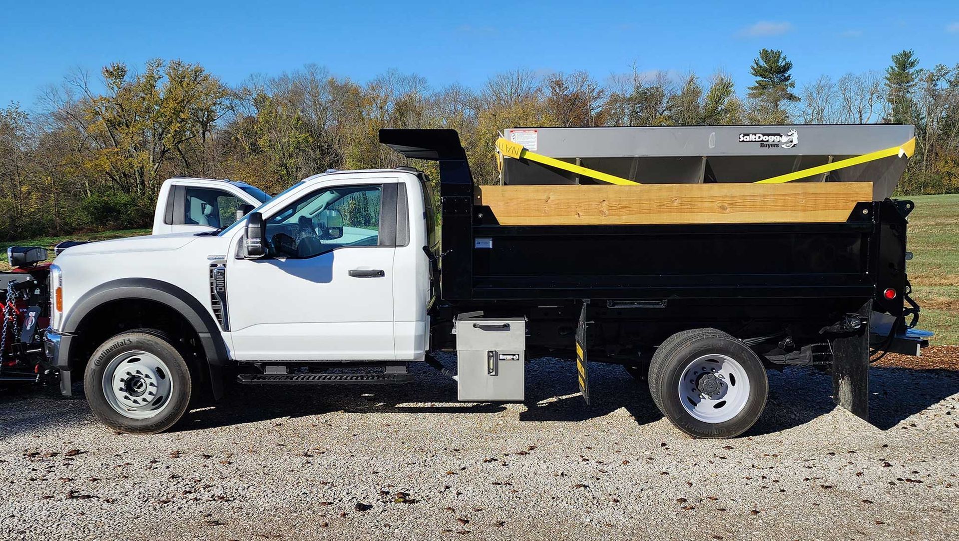 White dump truck with black bed, salt spreader, and snowplow.