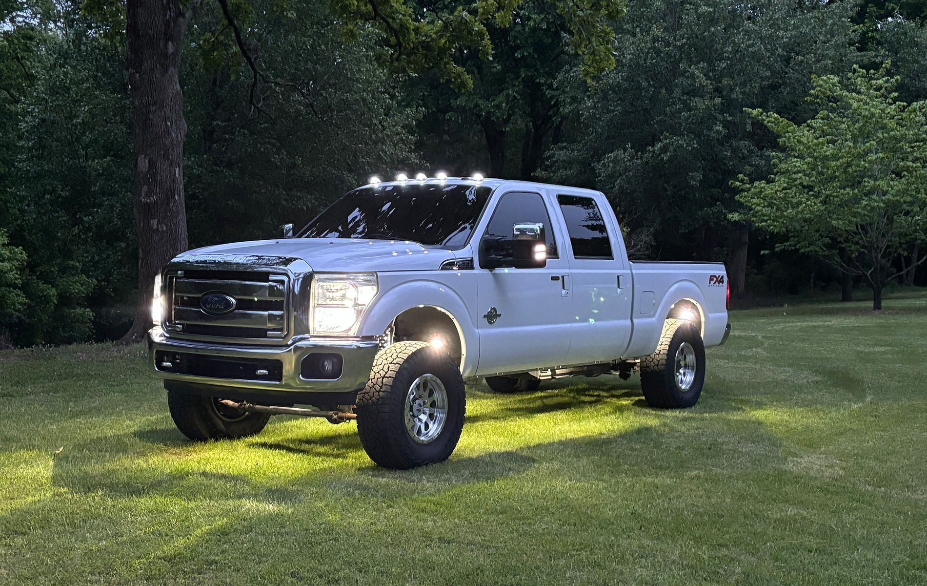 White pickup truck with LED lights parked on a green lawn at dusk.