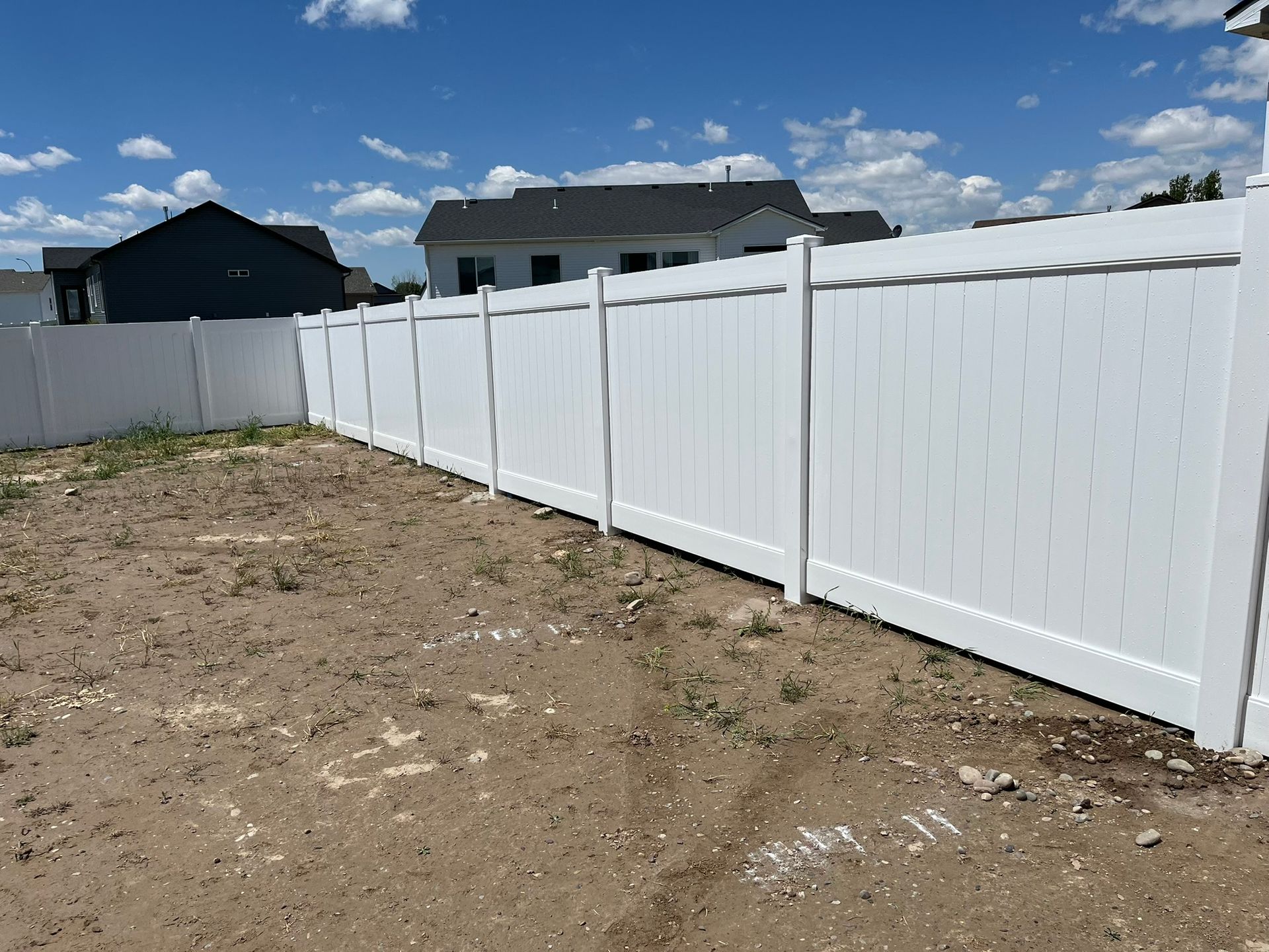 A white vinyl fence surrounds a dirt field in front of a house.