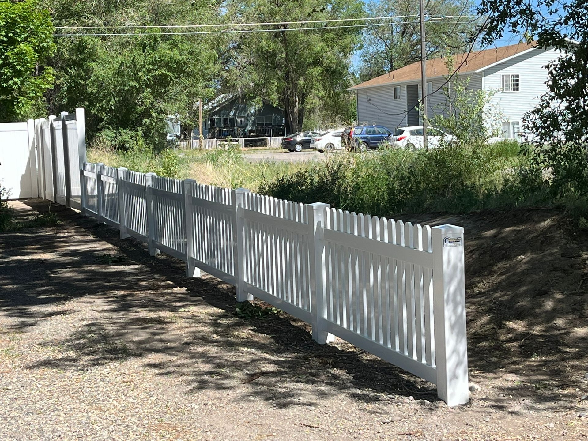 A white picket fence surrounds a gravel driveway in front of a house.