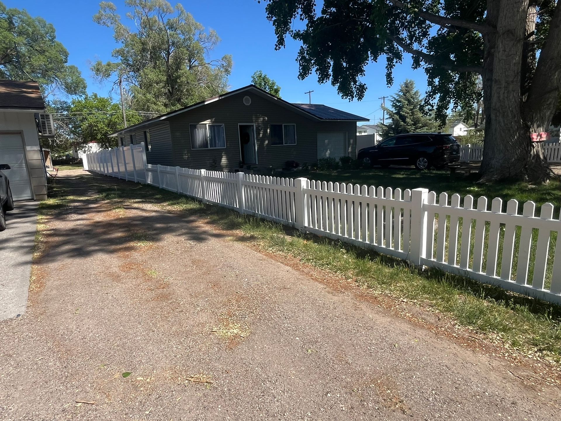A white picket fence surrounds a house on the side of a gravel road.