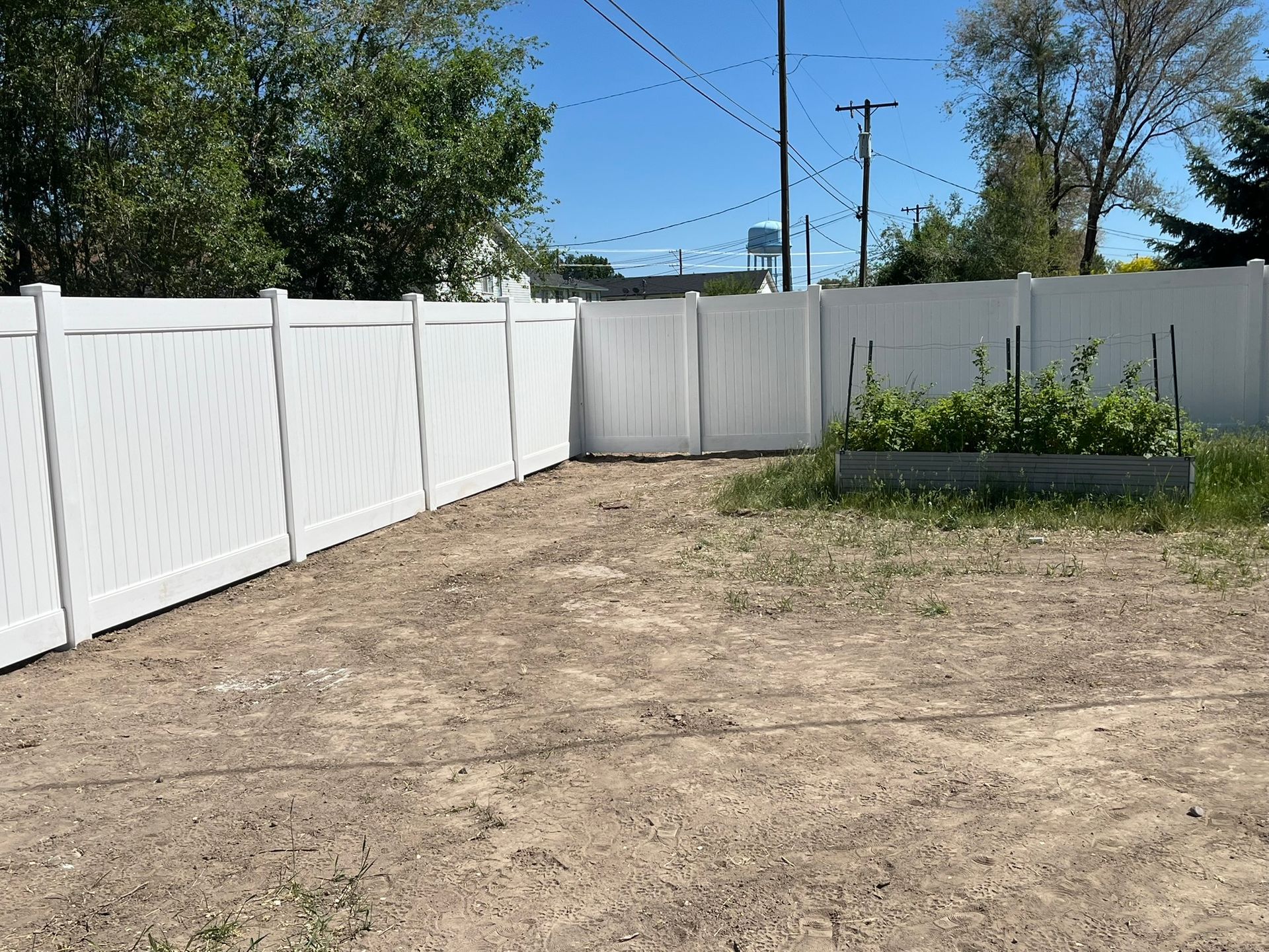 A white fence surrounds a dirt yard with trees in the background