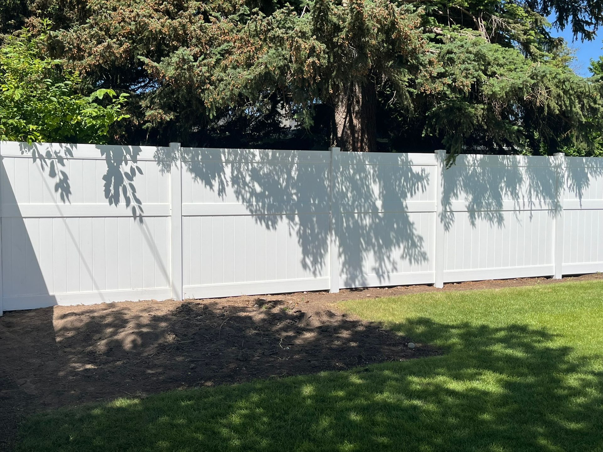 A white fence in a backyard with trees in the background.