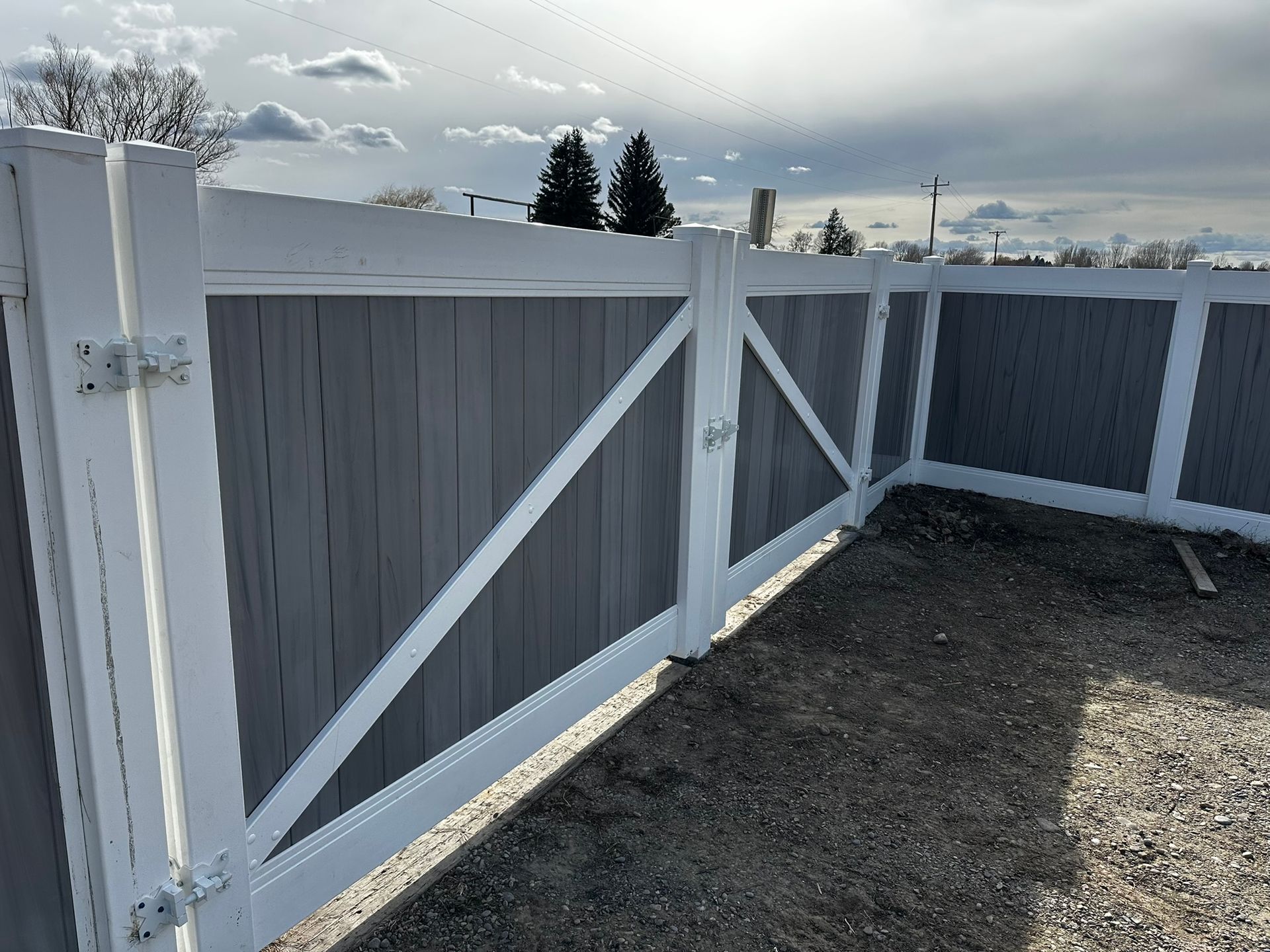 A white and gray fence with a gate in the middle of a dirt field.