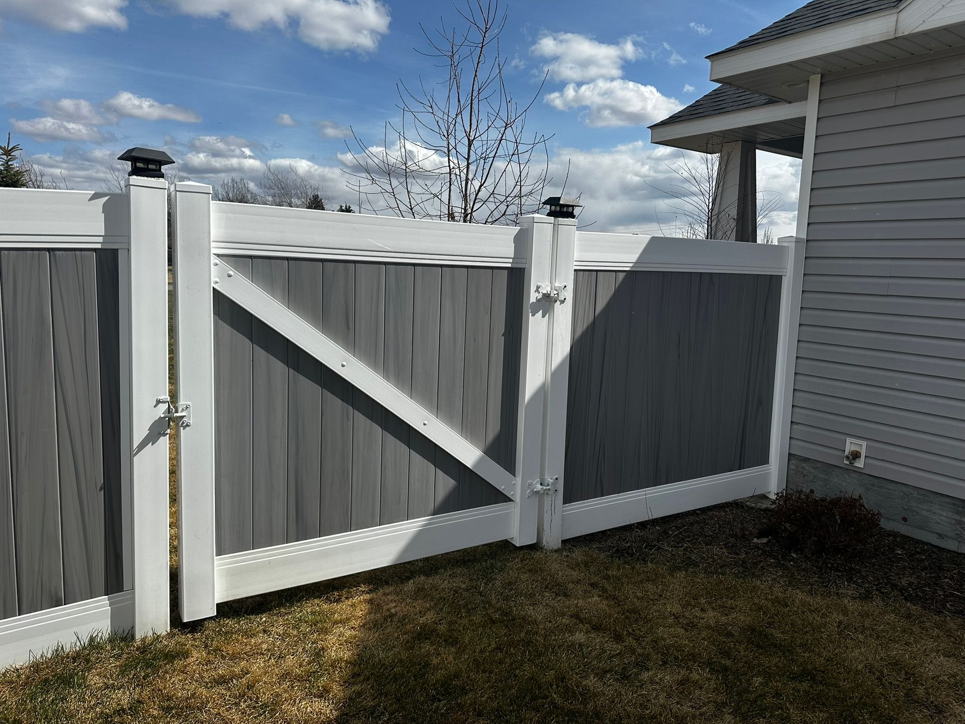 A white and gray fence with a gate in front of a house.