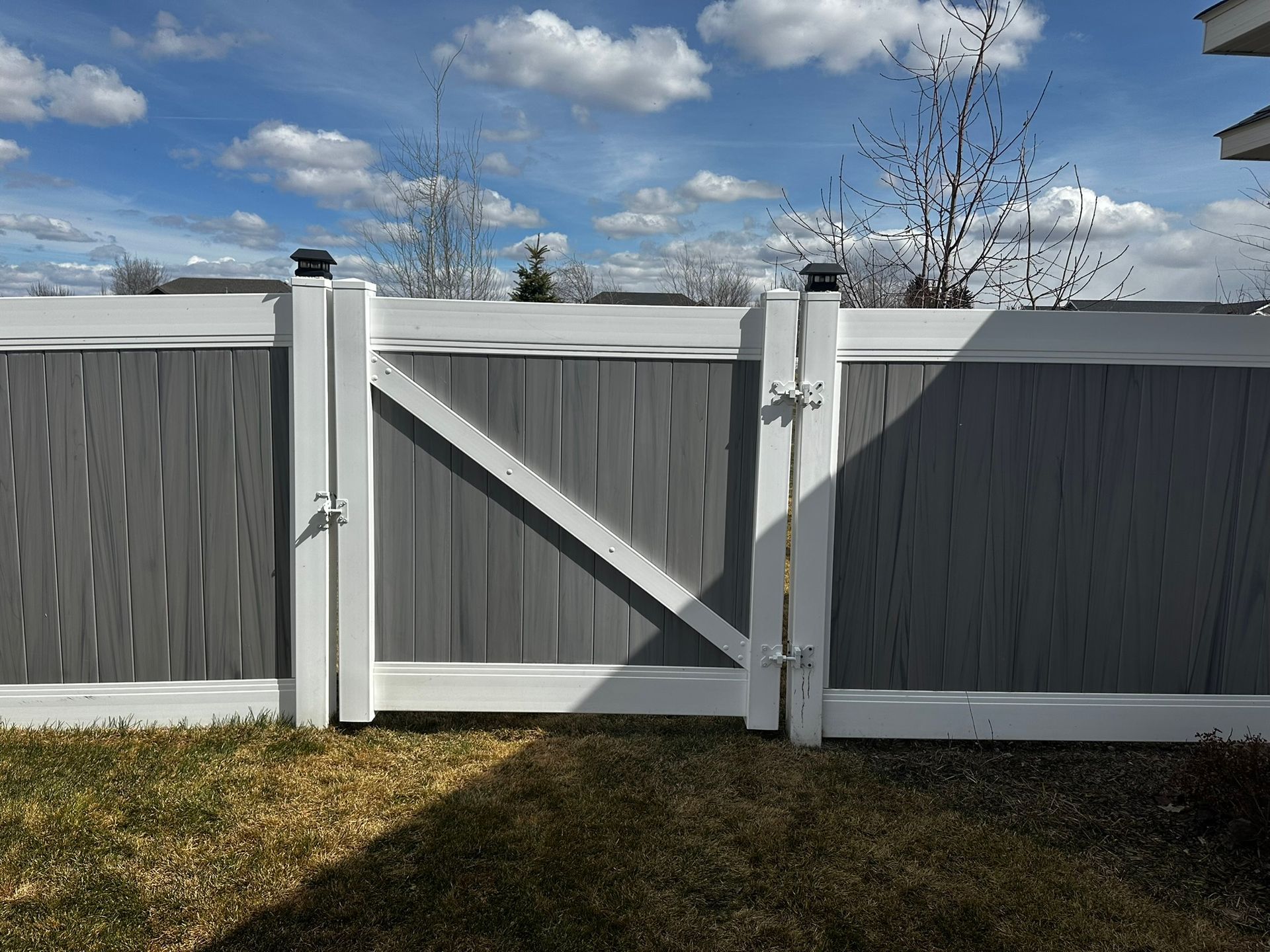 A gray and white fence with a white gate in the backyard.