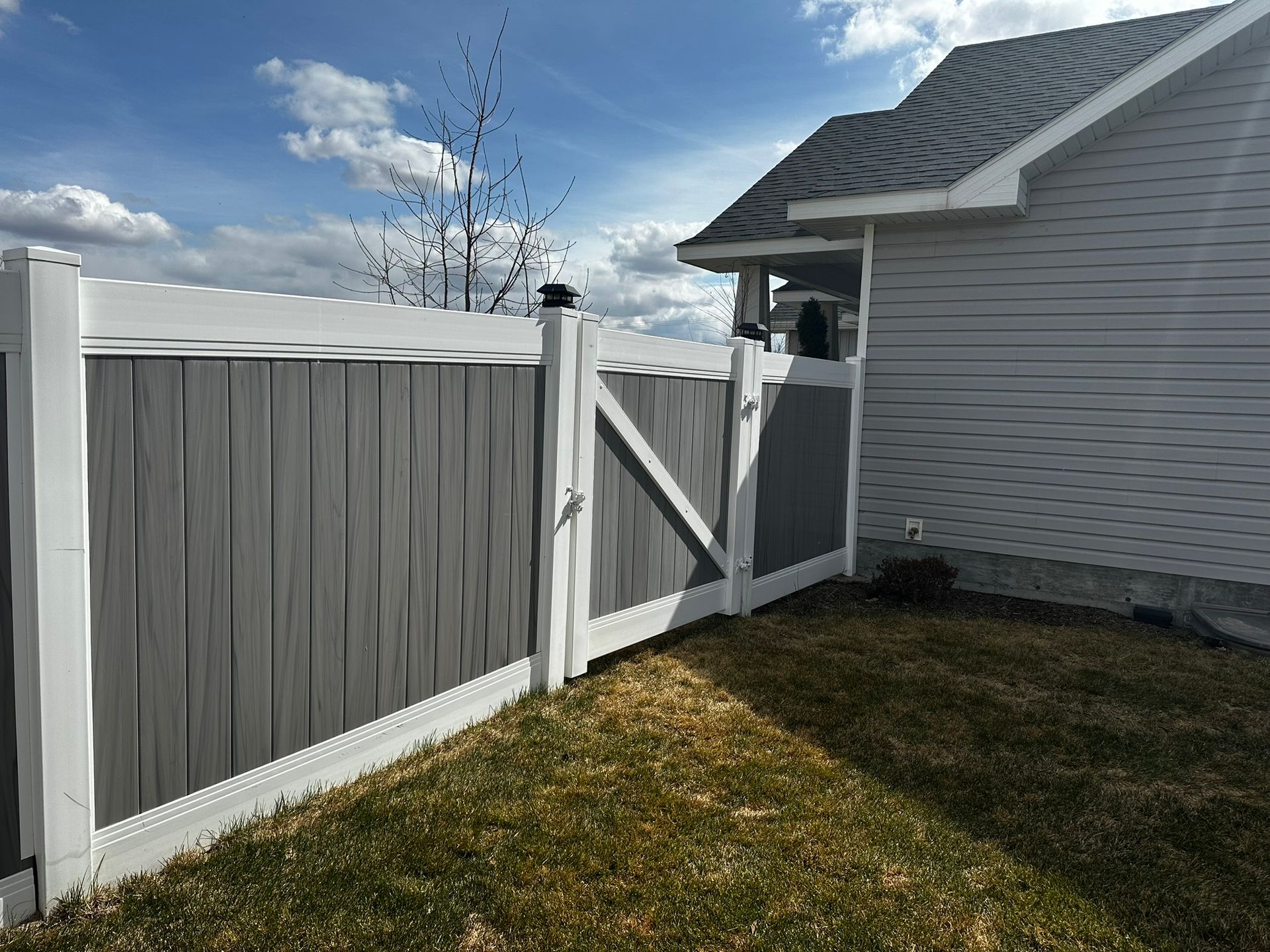 A gray and white fence is in front of a white house.