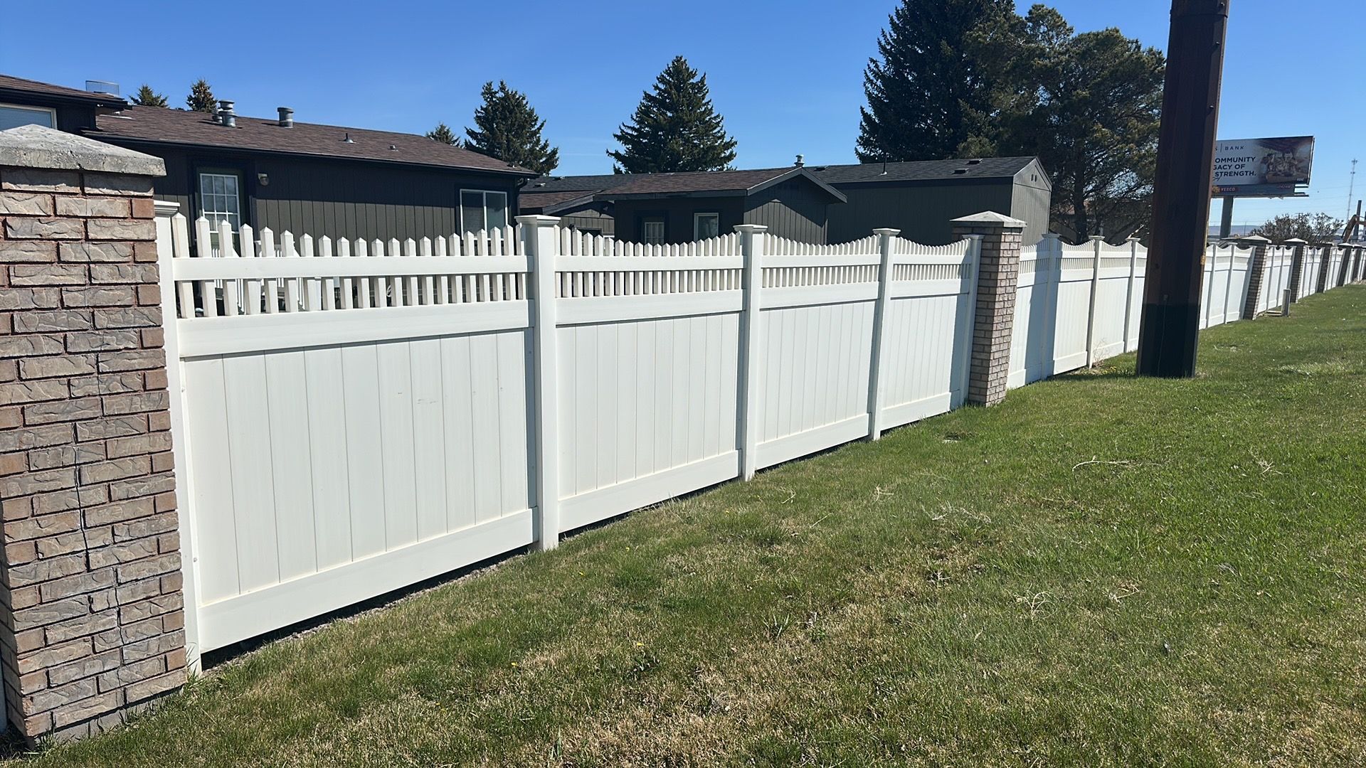 A white fence is surrounded by grass and brick pillars.